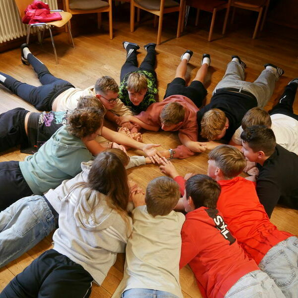 Kinder liegen auf dem Boden und spielen ein Kooperationsspiel&comma; bei dem sie sich gegenseitig an den Armen festhalten&period; 